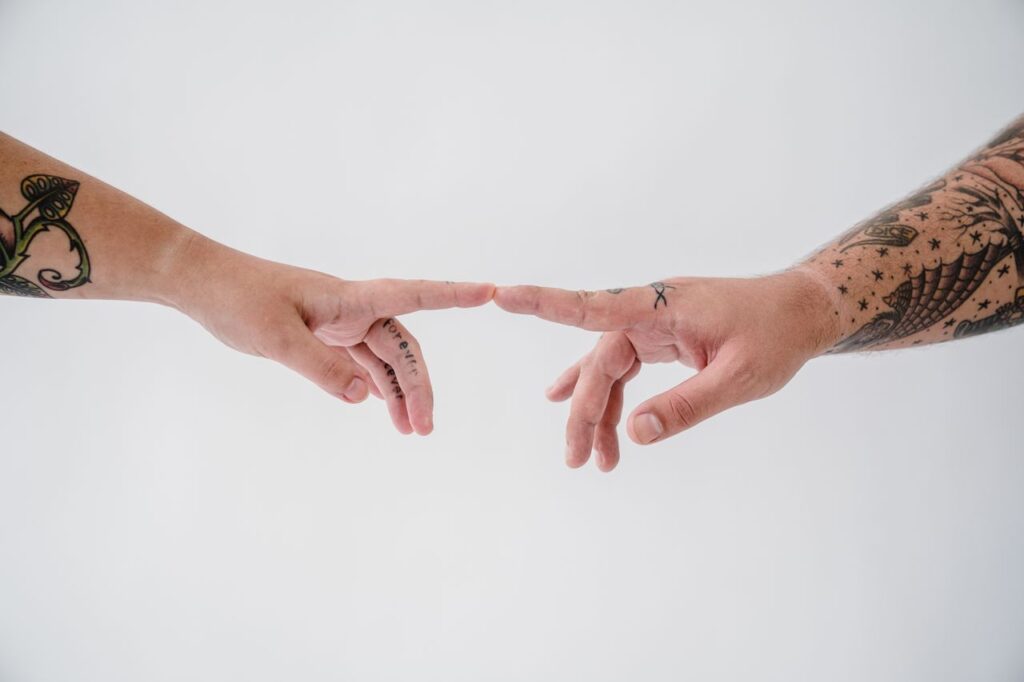 Two tattooed hands reaching out to each other in a minimalist studio setting, capturing a moment of connection.