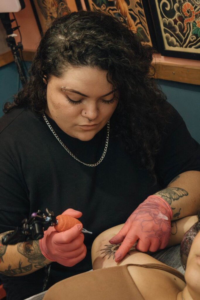 A skilled tattoo artist concentrates on tattooing a client's arm inside a studio with detailed wall art.