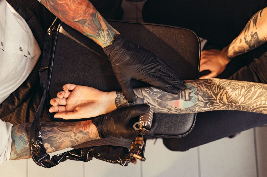 Tattoo artist applying detailed ink design on client's arm in a parlor.